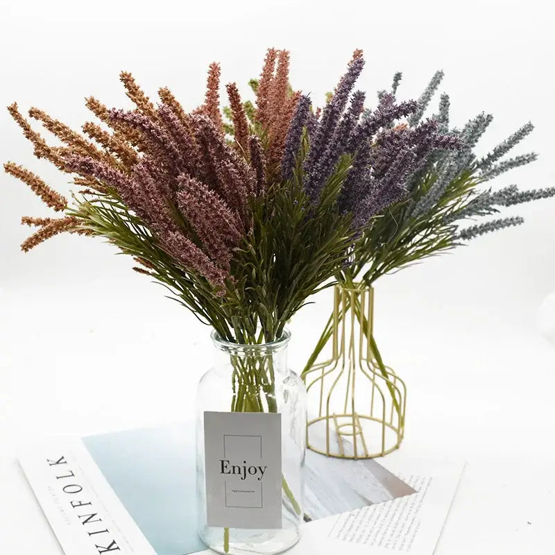 A bouquet of artificial lavender plants in purple mauve and brown shades arranged in a clear glass vase for decor