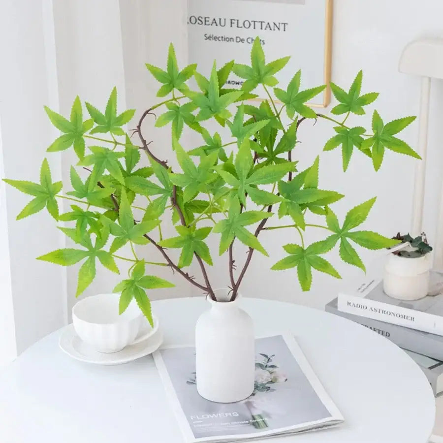 A white ceramic vase with a decorbites artificial maple leaf bouquet of green leaves on dark brown stems