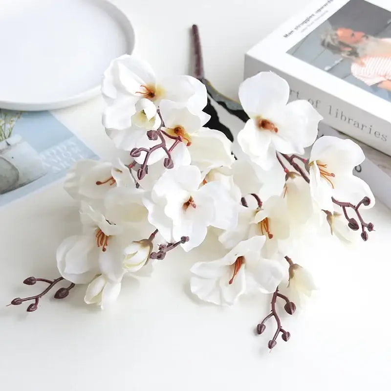 A cluster of white decorbites artificial orchid magnolia flowers with delicate petals and brownish stems in a natural bouquet