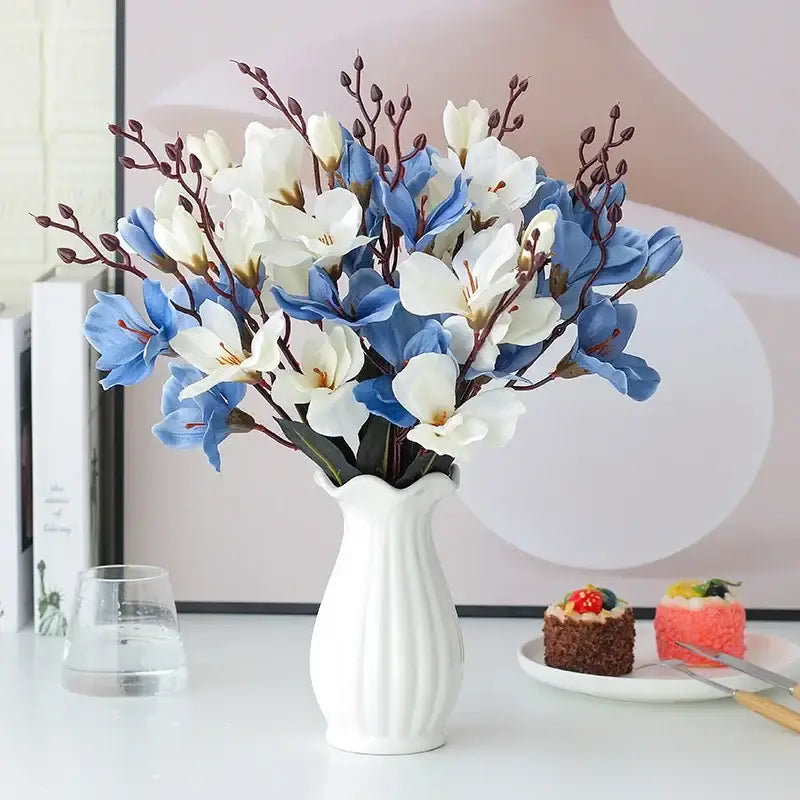 A white ceramic vase with vertical ridges holds a decorbites artificial orchid magnolia bouquet in blue and white colors