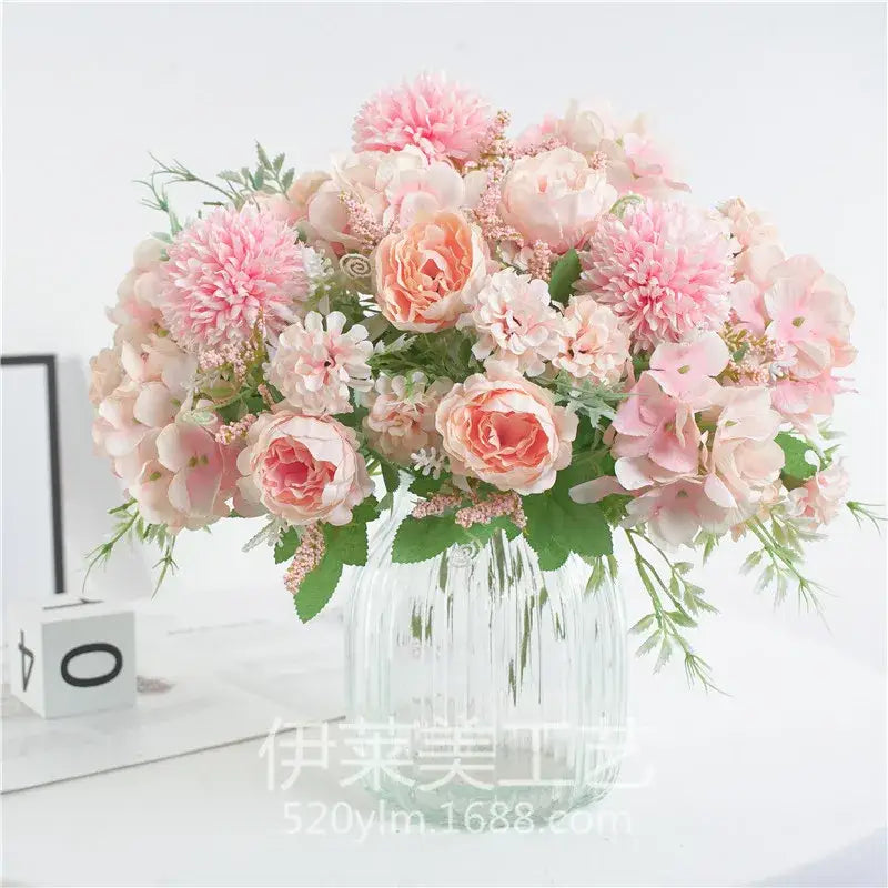 A decorbites artificial peony flower bouquet in soft pink and peach hues with greenery in a clear glass vase