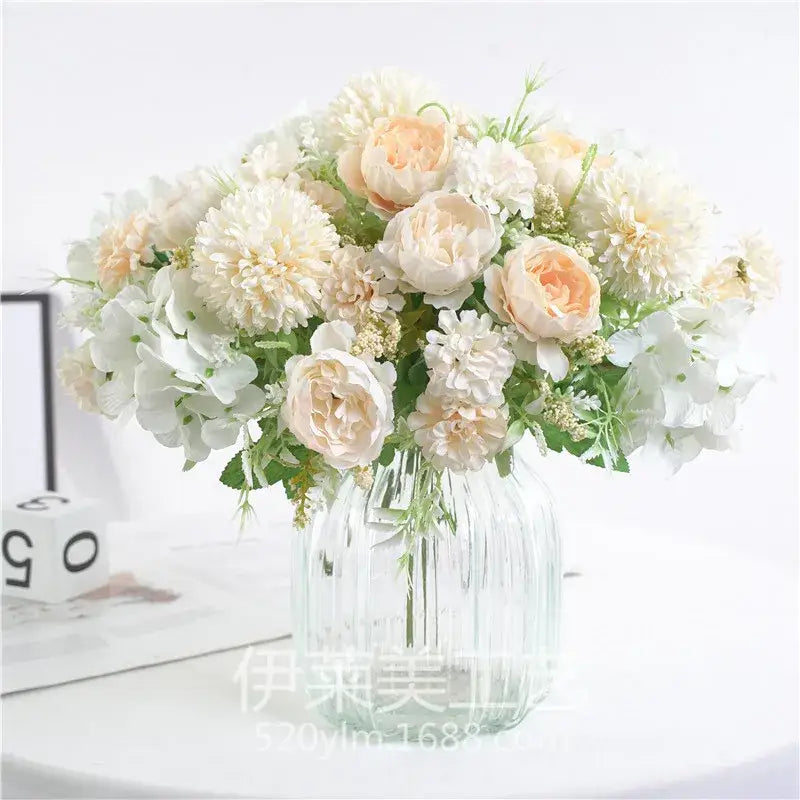 A decorbites artificial peony flower bouquet in soft cream and peach tones displayed in a clear ridged glass vase