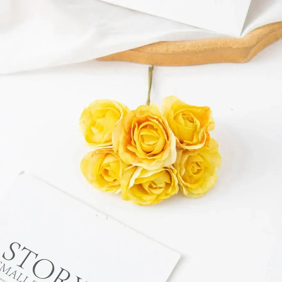 A cluster of five yellow decorbites artificial rose bouquet with delicate petals and green stems for home decor and weddings