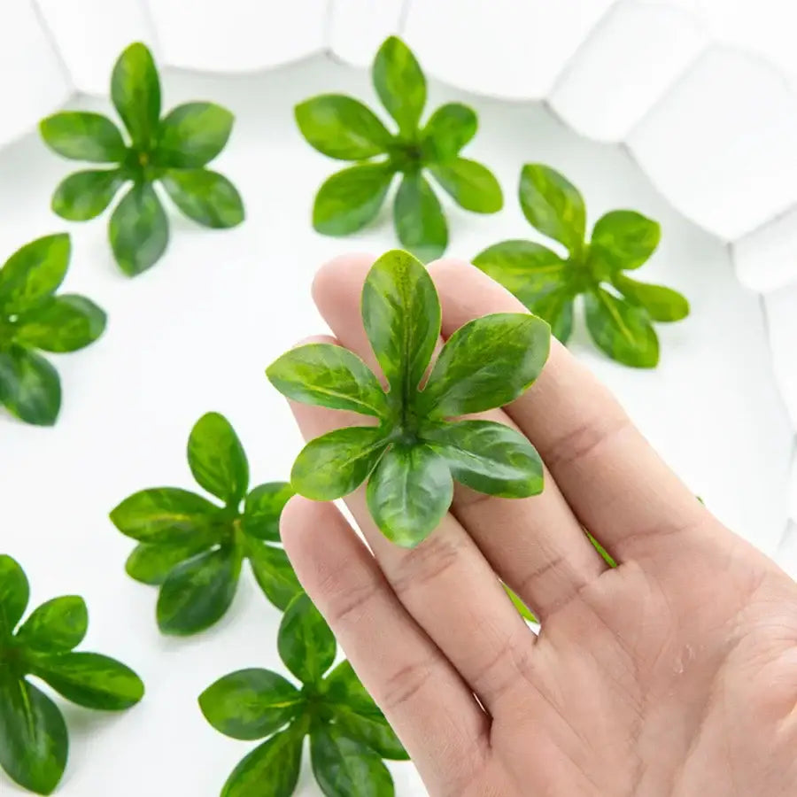 A hand holds a small green decorbites artificial rose leaf with five lobes and subtle veining for DIY wreaths