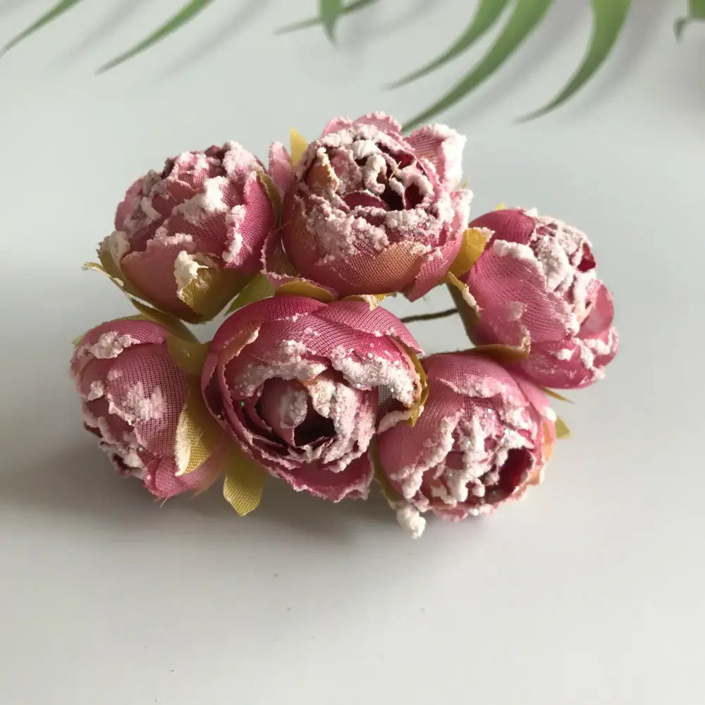 A cluster of five pink decorbites artificial roses with textured fabric petals and yellow-green stems for bridal décor