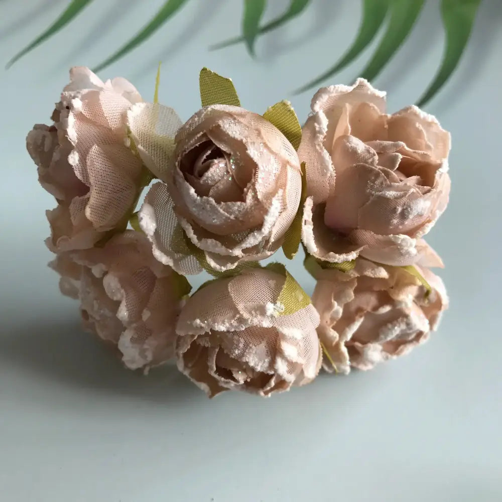 A delicate cluster of blush pink decorbites artificial roses with lace detailing and green ribbons for bridal use