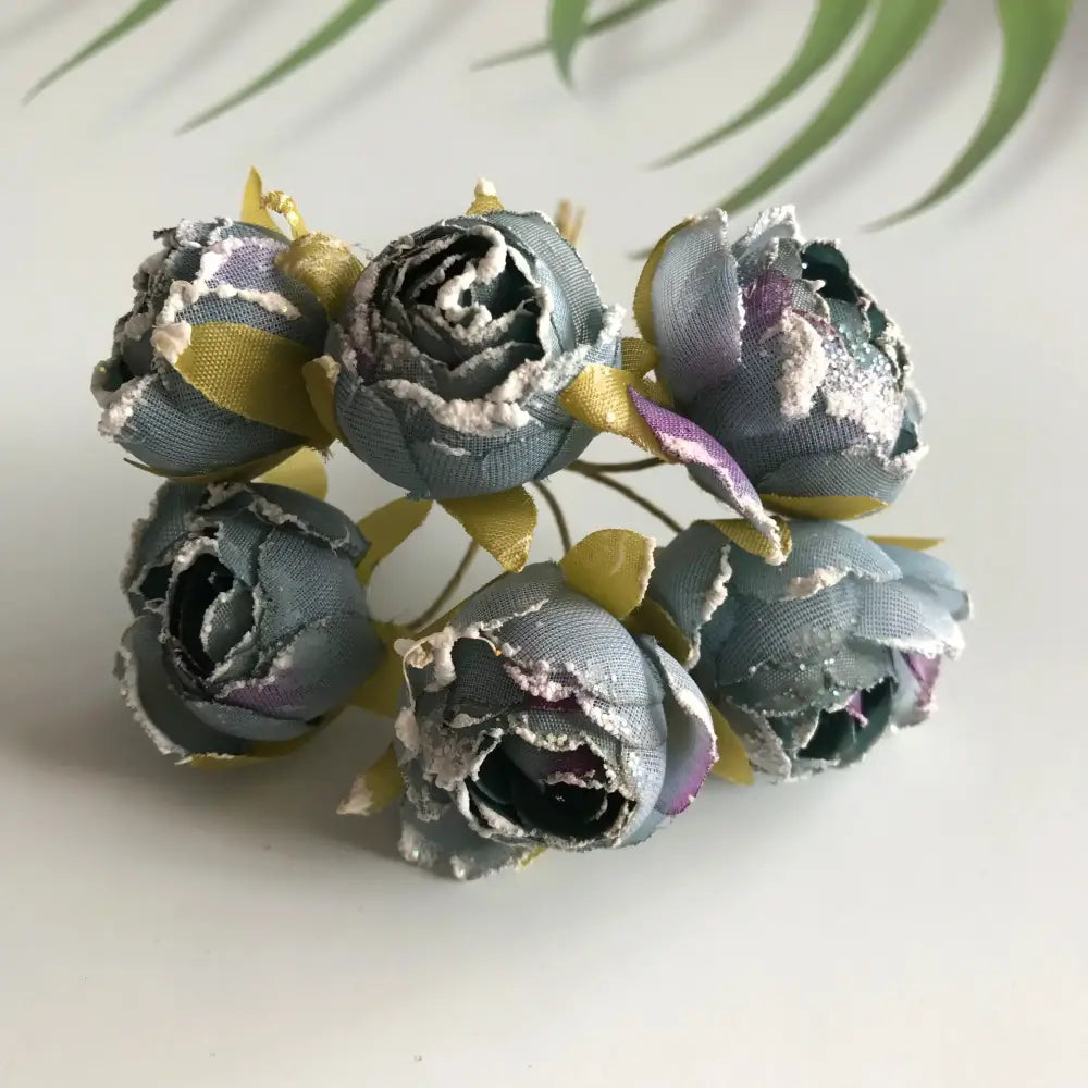 A cluster of decorbites artificial roses bridal bouquet in muted gray fabric with purple white accents and yellow green leaves