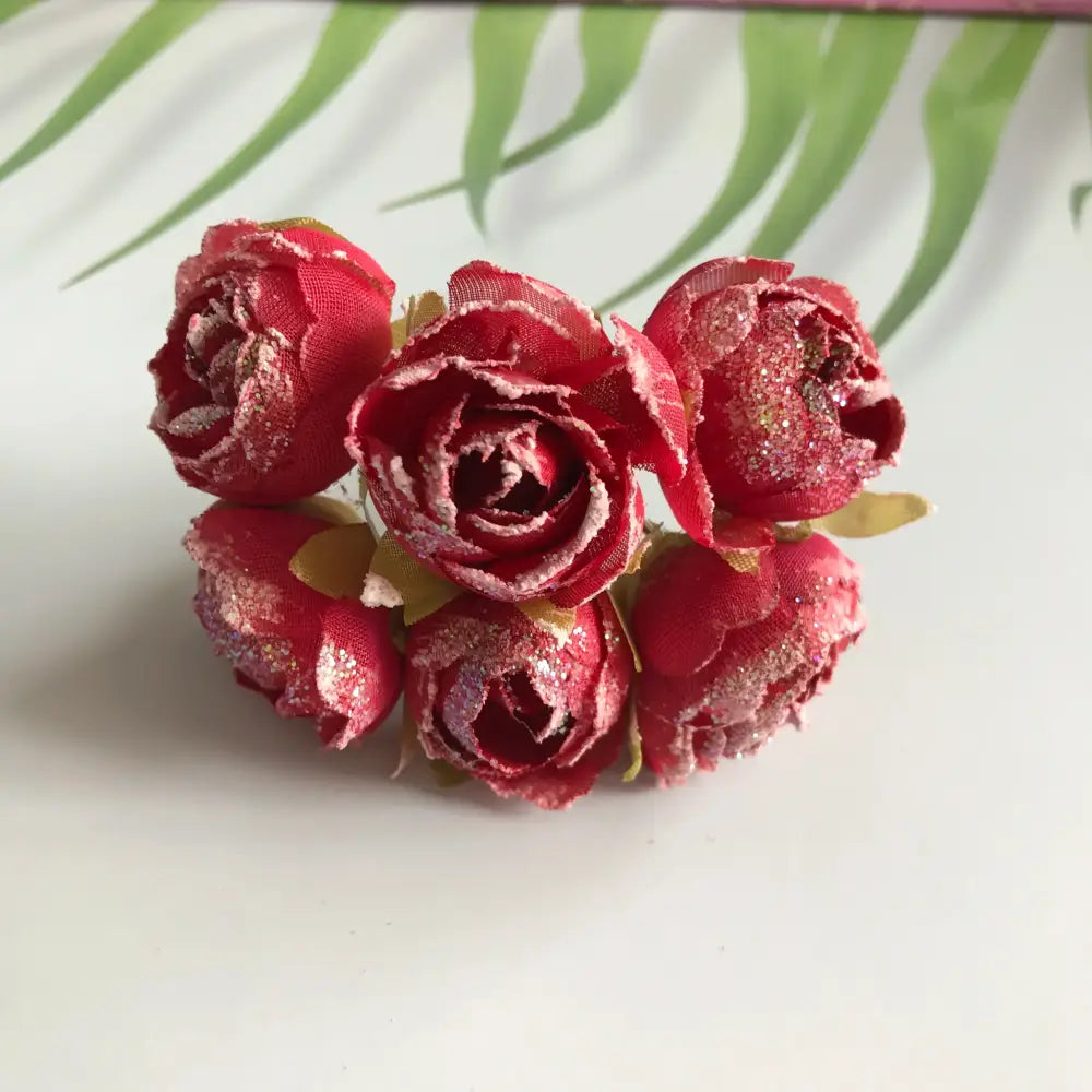 A cluster of five vibrant red decorbites artificial roses with glitter finish and gold leaf accents for bridal decoration