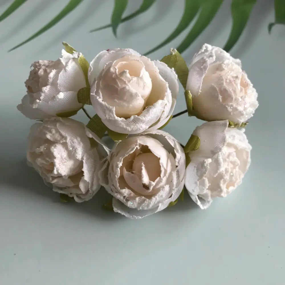 A cluster of six delicate ivory decorbites artificial roses fabric peonies with subtle glitter and green ribbon stems for bridal use