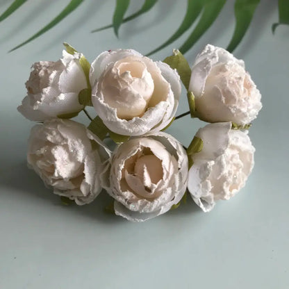 A cluster of six delicate ivory decorbites artificial roses fabric peonies with subtle glitter and green ribbon stems for bridal use