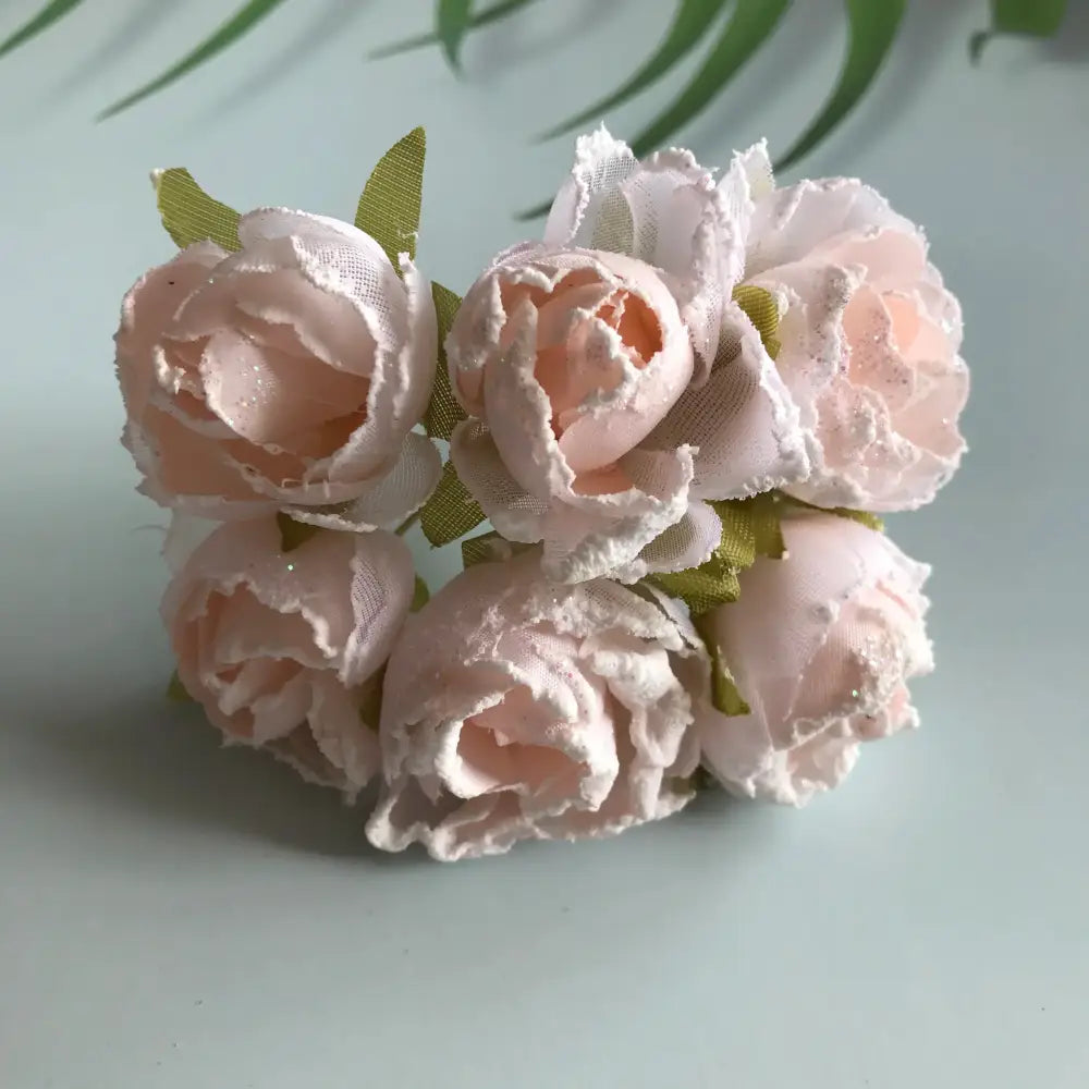 A delicate cluster of pale pink decorbites artificial roses with glitter accents and green ribbon stems for bridal use