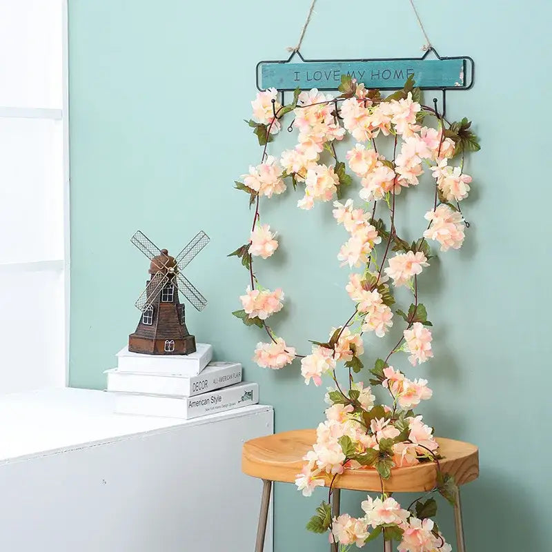 A delicate peach-colored decorbites artificial sakura flowers vine with green leaves hanging from a rustic teal sign