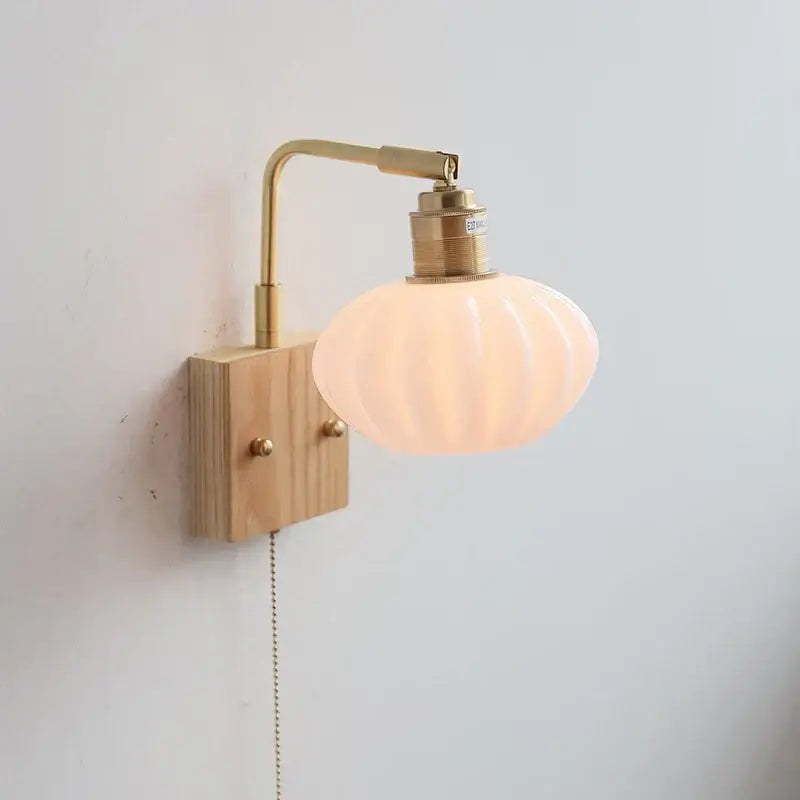 Decorbites ash wood wall light with a warm peach glass shade and brass hardware mounted on an ash wood fixture