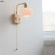 A warm-toned brass wall light with ash wood base and off-white ribbed glass shade from DecorBites ash wood collection