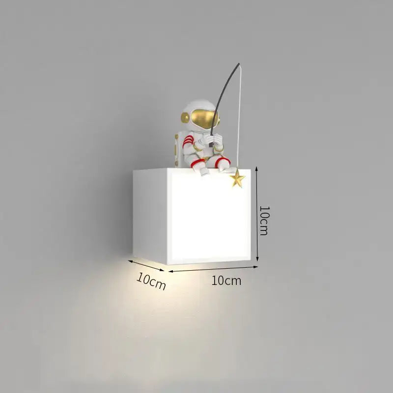 White cube-shaped wall lamp with gold-accented astronaut figurine fishing on top for decorbites astronaut cartoon sconce