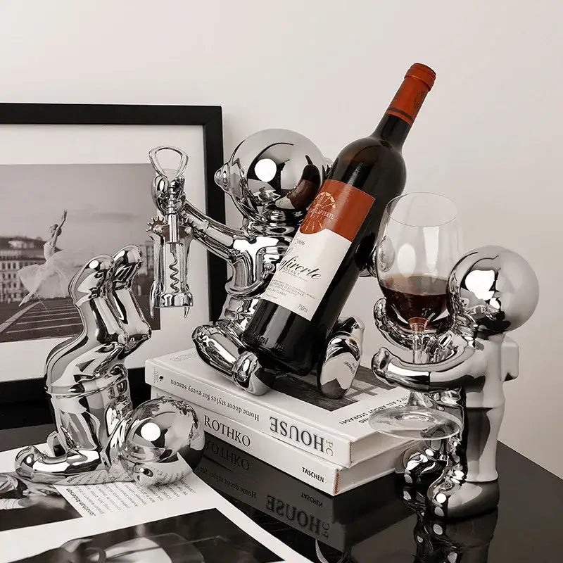 Shiny chrome decorbites astronaut ceramic wine rack with playful humanoid figurines holding wine bottle and glass