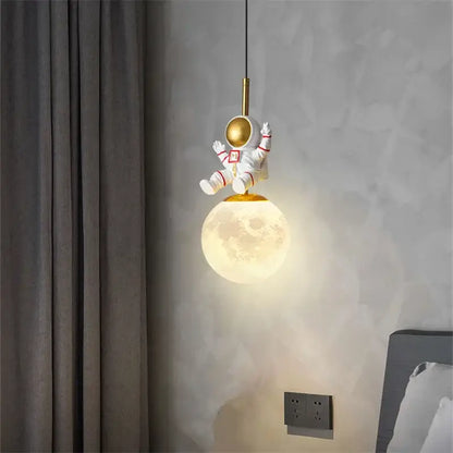 Decorbites astronaut chandelier featuring a white figurine with gold helmet and red accents above glowing moon lamp