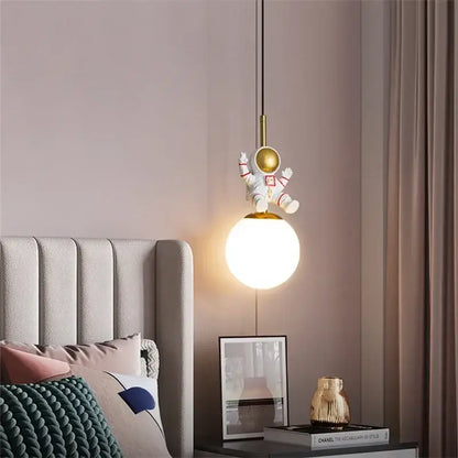 A whimsical white and gold decorbites astronaut chandelier with a glowing spherical lamp for personalized kids room decor