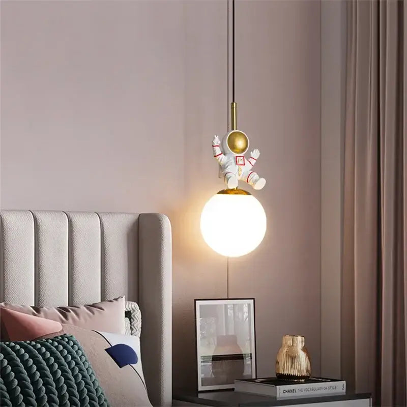 A whimsical white and gold decorbites astronaut chandelier with a glowing spherical lamp for personalized kids room decor