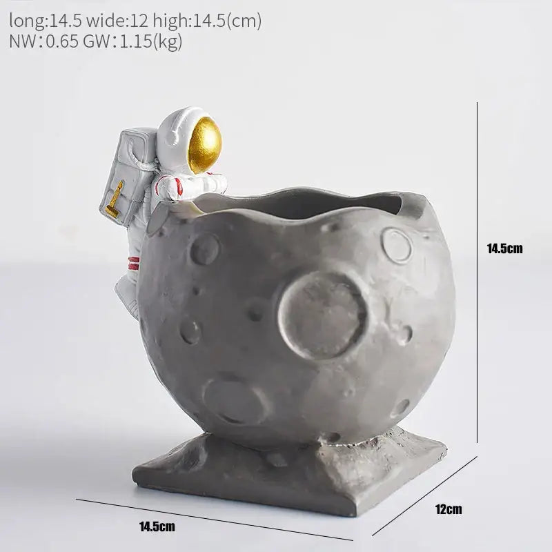 Gray resin moon-shaped pen holder with white astronaut figurine featuring gold visor and backpack details for desk use