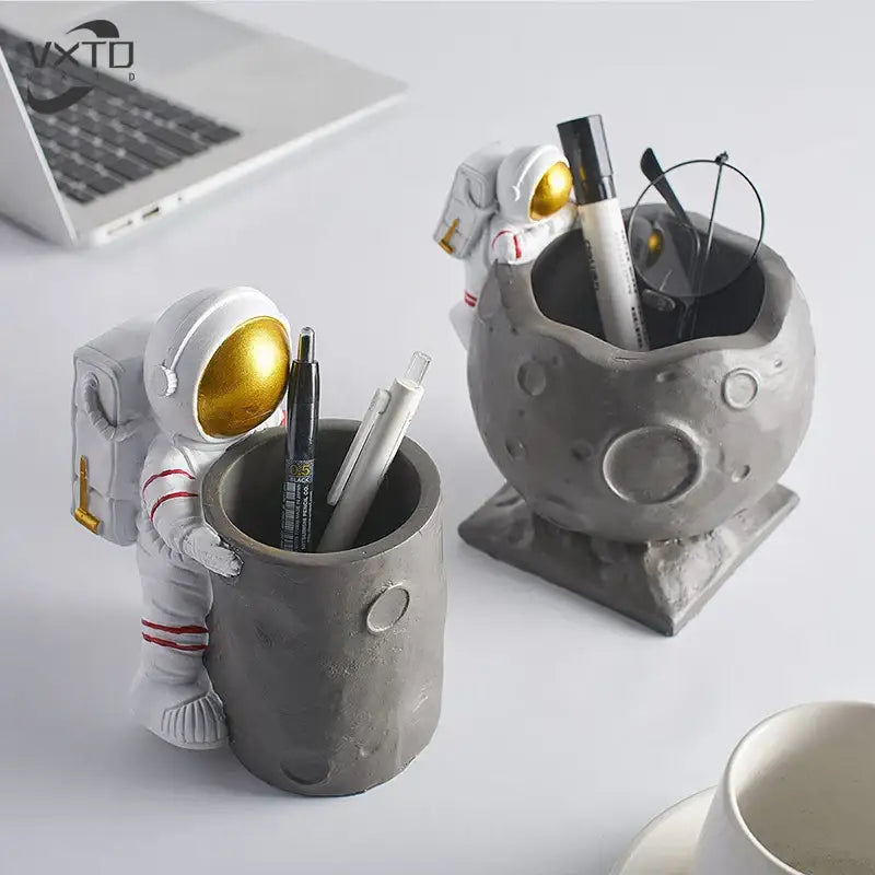 White astronaut figurine with gold visor and red-striped suit holding gray cratered moon pen holder figurines for desk decor