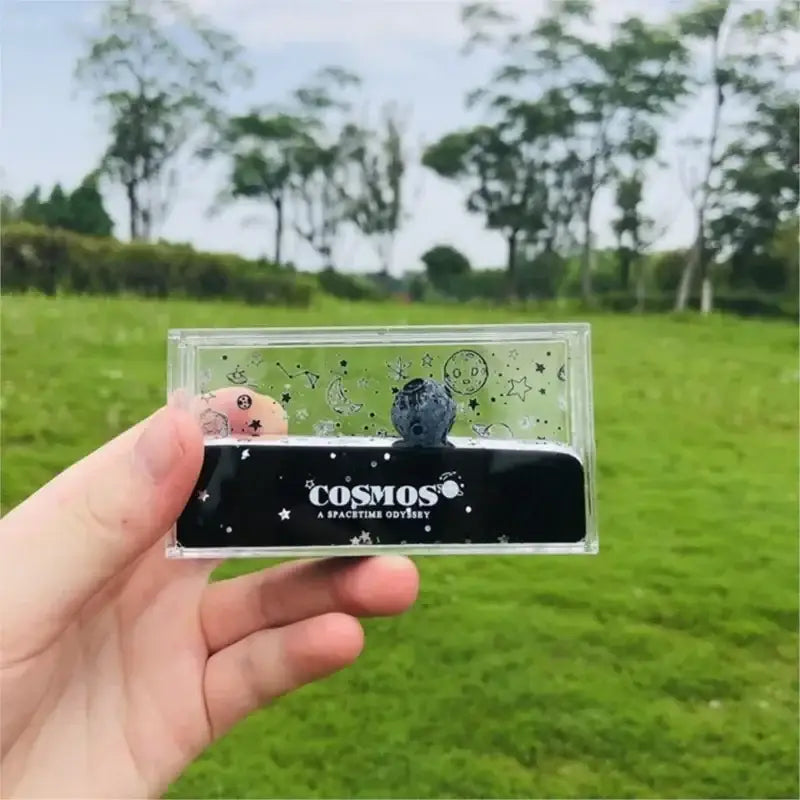 A clear rectangular case holding a dark blue textured sphere with celestial illustrations from decorbites astronaut drift keychain collection