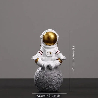 White astronaut figurine with gold helmet sitting in meditation pose on textured gray moon surface by DecorBites astronaut figurines