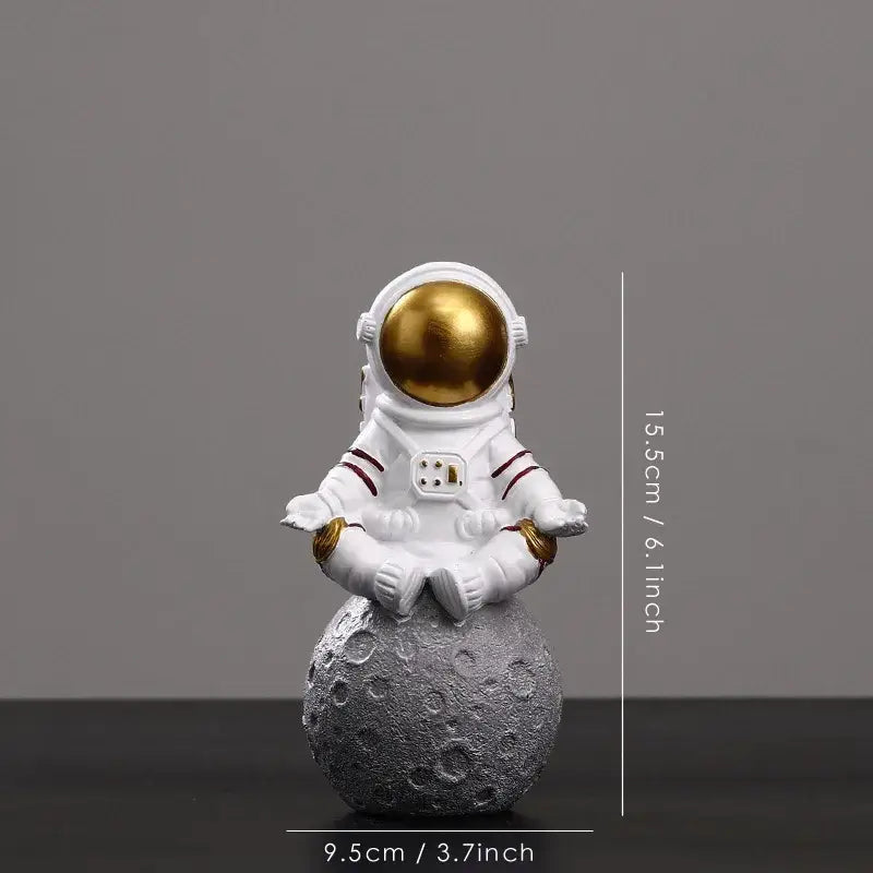White astronaut figurine with gold helmet sitting in meditation pose on textured gray moon surface by DecorBites astronaut figurines