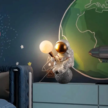 White resin decorbites astronaut led desk lamp with gold helmet seated on gray moon surface holding glowing lamp