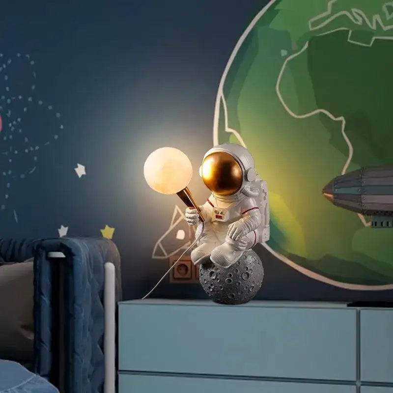 White resin decorbites astronaut led desk lamp with gold helmet seated on gray moon surface holding glowing lamp