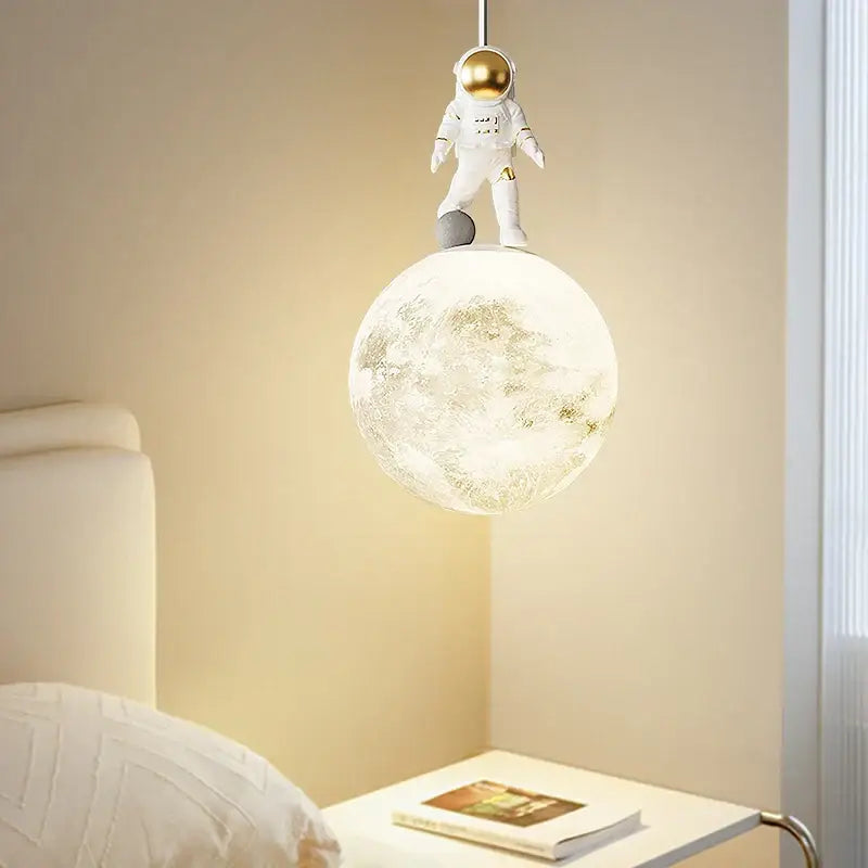 A decorbites astronaut lunar pendant light featuring a white astronaut figurine with a gold helmet on a textured moon lamp