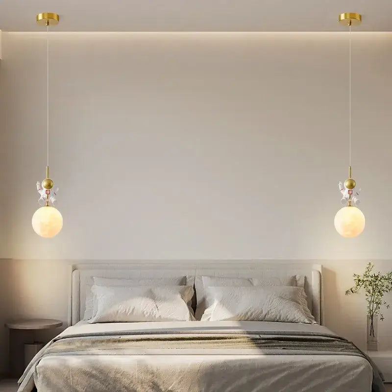 Gold-finished decorbites astronaut moon pendant light with spherical frosted glass and figurine accents above bed