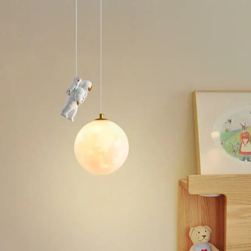 White astronaut figurine hanging above a glowing moon-shaped pendant light decorbites astronaut moon for childrens room