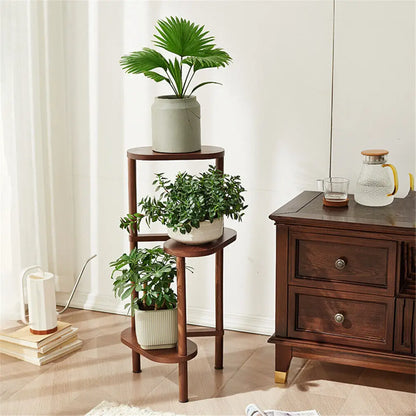 Dark wood bamboo tall corner plant stand with three circular shelves and slender legs holding green plants in ceramic pots