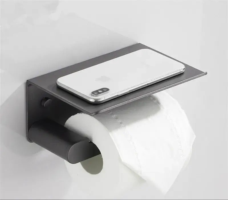 Black metal toilet paper holder with integrated shelf holding a silver smartphone from decorbites bathroom hardware set