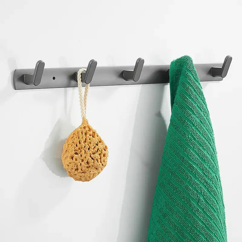 Gray metal wall-mounted hook rack with five hooks holding green towel and beige loofah from decorbites bathroom hardware set