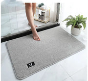 Gray plush decorbites bathroom mat with soft textured surface, subtle stitched border, and black embroidered logo patch