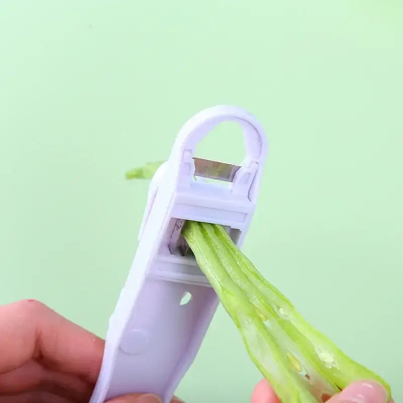 White plastic decorbites bean slicer cutter with metal blade peeling a green bean as slicer cutter peeler tool