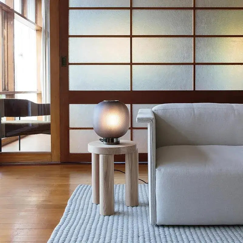 A softly glowing black glass ball table light by decorbites on a wooden side table for bedroom and living room use