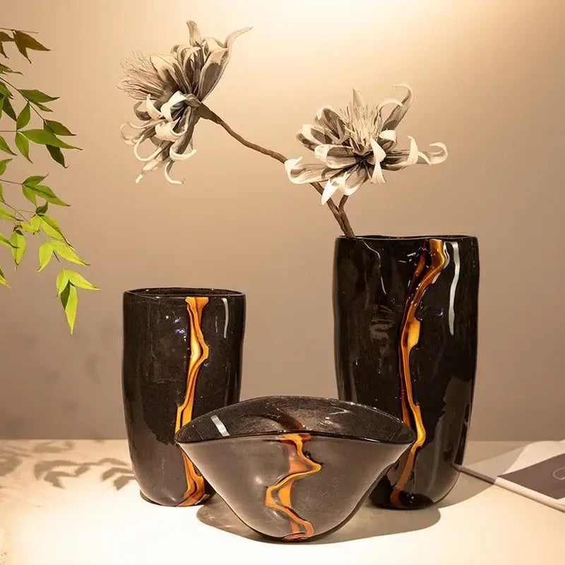 Set of three decorbites black glass vases with golden-orange marbled accents holding delicate white flowers for decoration