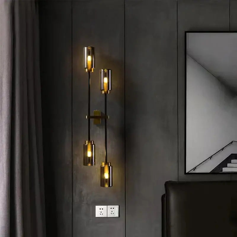Modern brass-finished decorbites black glass wall lamp with four cylindrical glass shades emitting warm glow
