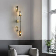 Modern brass-finished decorbites black glass wall lamp with four cylindrical shades emitting warm light for living room decor