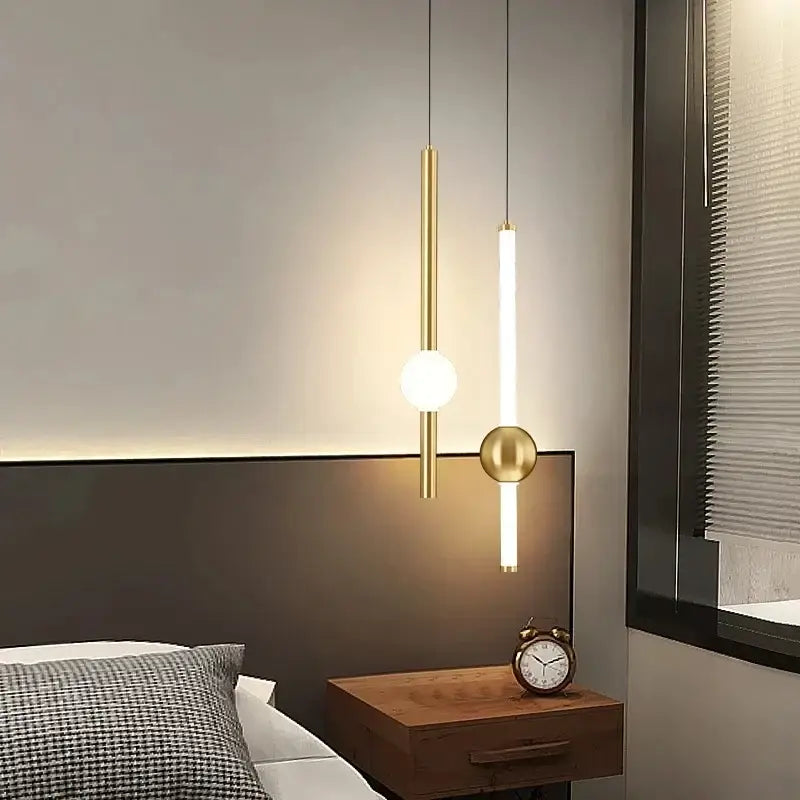 Two modern decorbites black gold ceiling pendant lights with gold cylindrical rods and spheres hanging above a bed