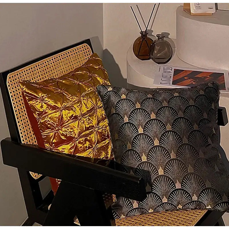 Two decorative throw pillow cases in black and gold featuring quilted and vintage italian luxury fan patterns on a chair