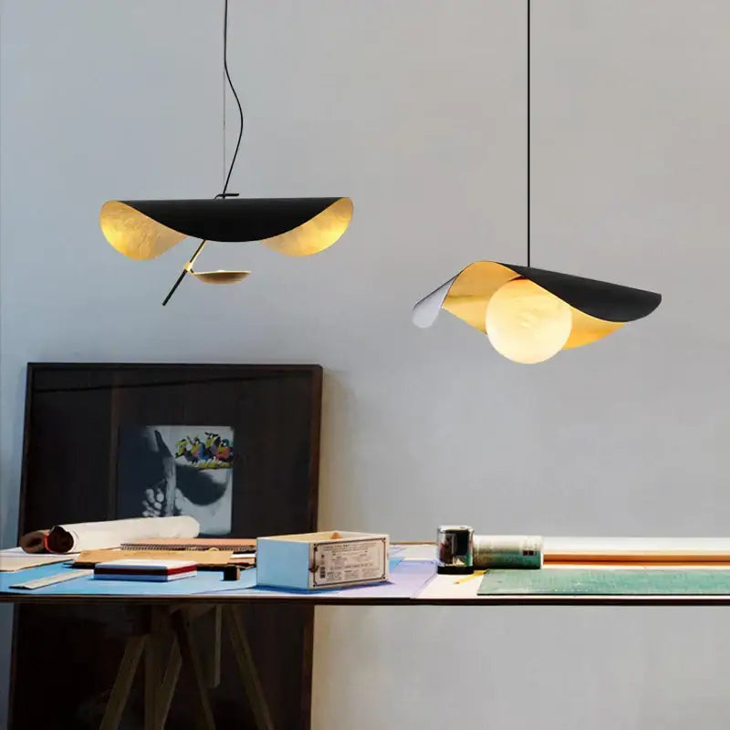 Two decorbites black gold pendant lights with leaf-like glass shades hang above a desk in retro Nordic style
