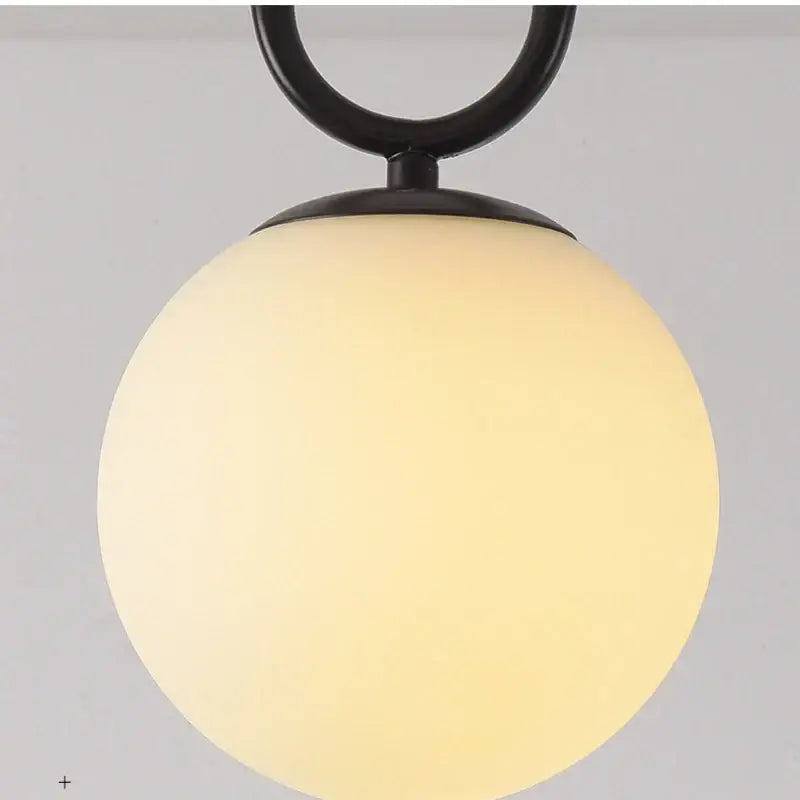 A sleek black gold glass ceiling lamp by DecorBites with a suspended glowing off-white spherical pendant light