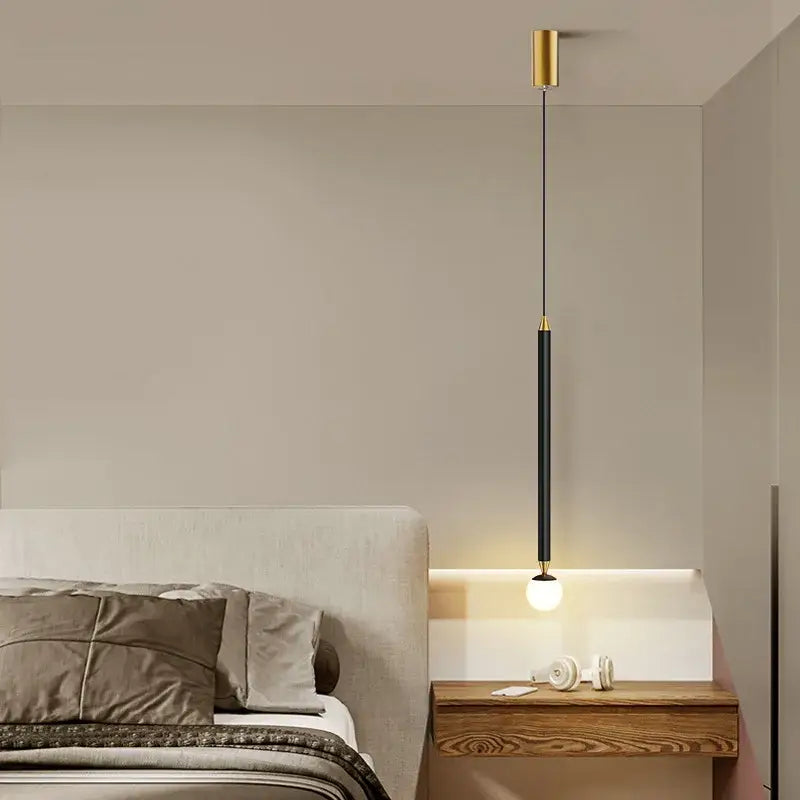 A sleek black gold hanging pendant light by DecorBites with cylindrical design suspended above wooden nightstand