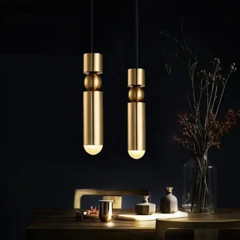 Two sleek gold led tube pendant lamps from decorbites black gold with black cords against a dark backdrop