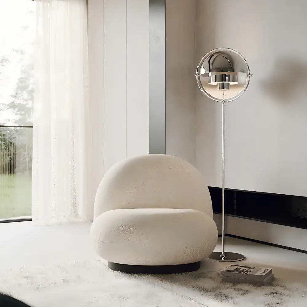 Cream-colored plush spherical armchair with black circular base paired with decorbites black gold metal floor lamp for modern décor