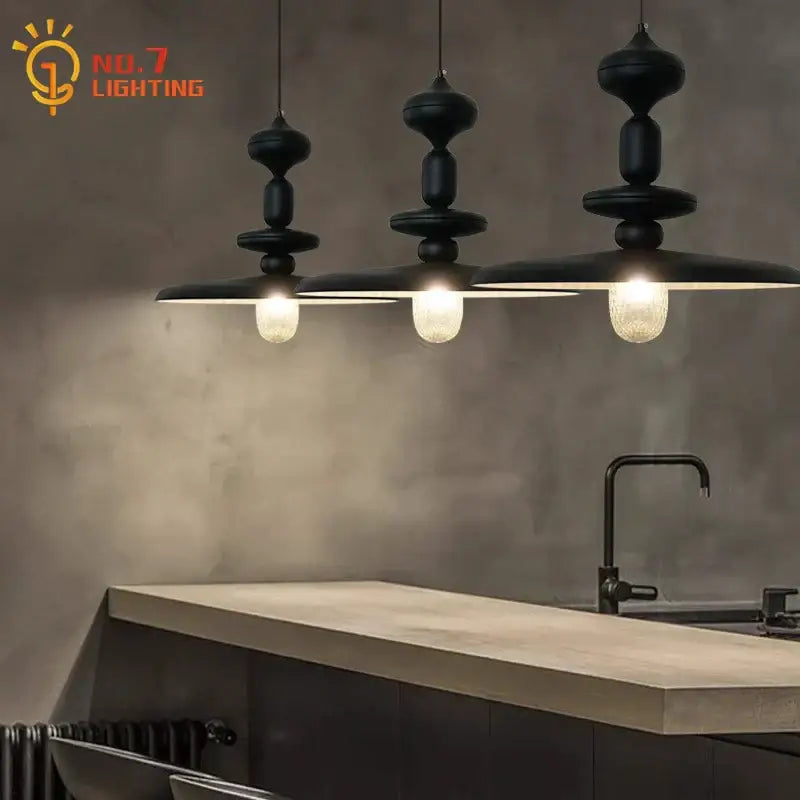 Three black sculptural decorbites black gyroscope pendant lights with textured glass bulbs hang above a kitchen counter
